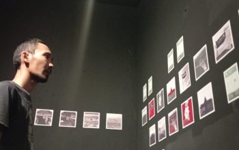 Seorang pengunjung berdiri dalam diam, mengamati susunan foto bertajuk SISA yang menempel di dinding hitam. Potongan-potongan visual tentang Teluk Palu dan pegunungan di sekitarnya tersusun seperti cerita yang tak selesai, menghadirkan refleksi sunyi tentang alam yang perlahan berubah dan menyisakan jejak ingatan.